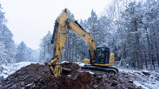 Caterpillar excavator using Trimble Siteworks machine guidance in snowy forest construction site