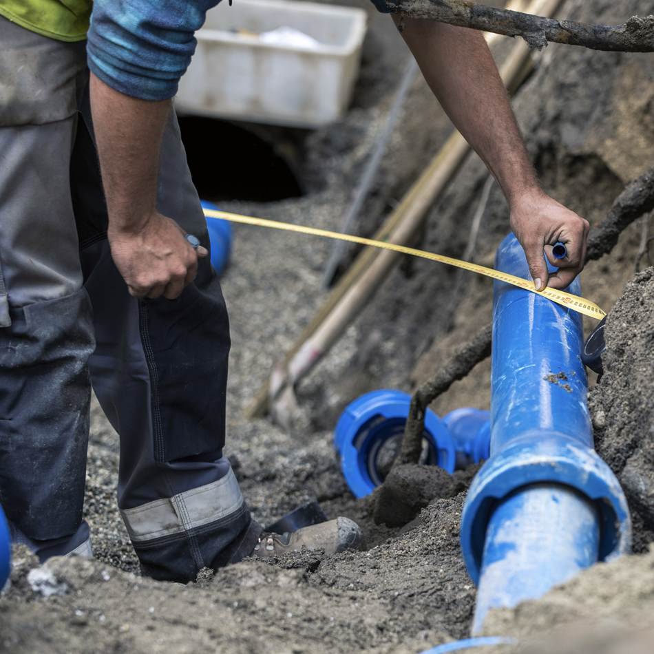 A man in a ditch with a measuring tape, working on a pipe installation project.