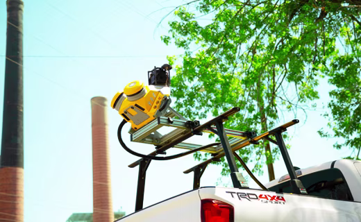 Trimble MX50 移动影像测绘系统安装在一辆白色 SUV 车顶部，旁边是绿色树枝和高大的红砖烟囱结构。