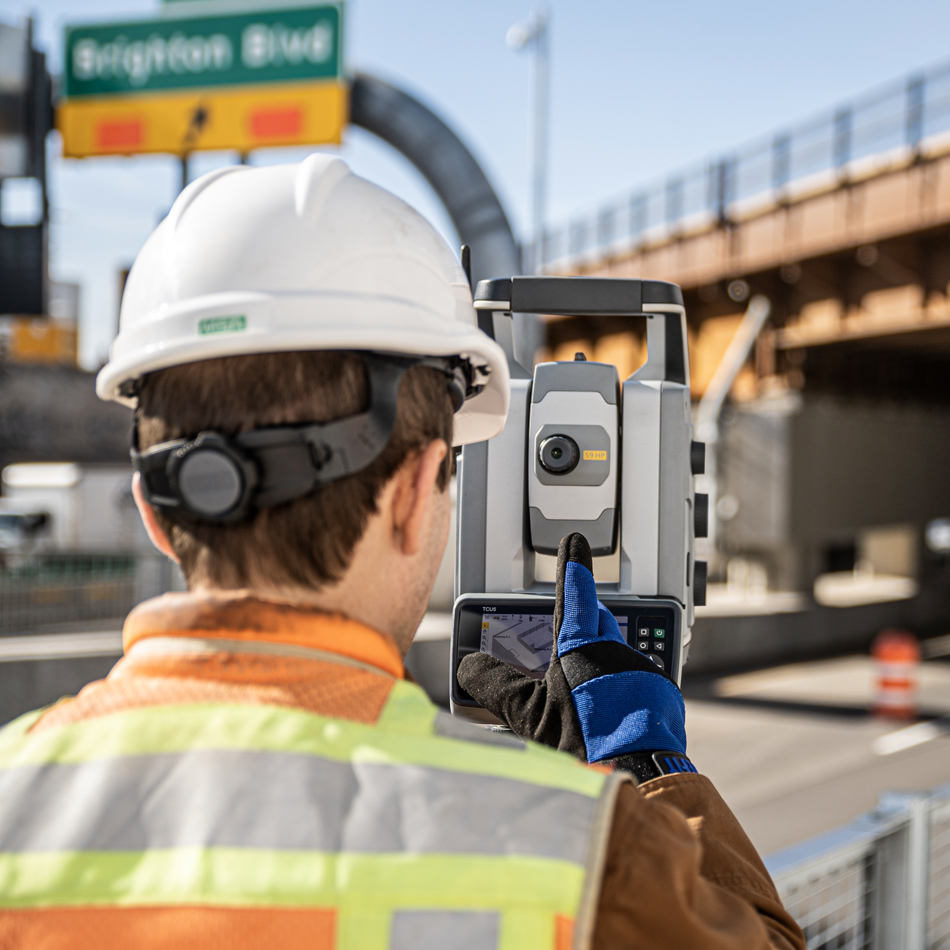 Worker in vest and hard hat using Trimble S9 total station near a bridge