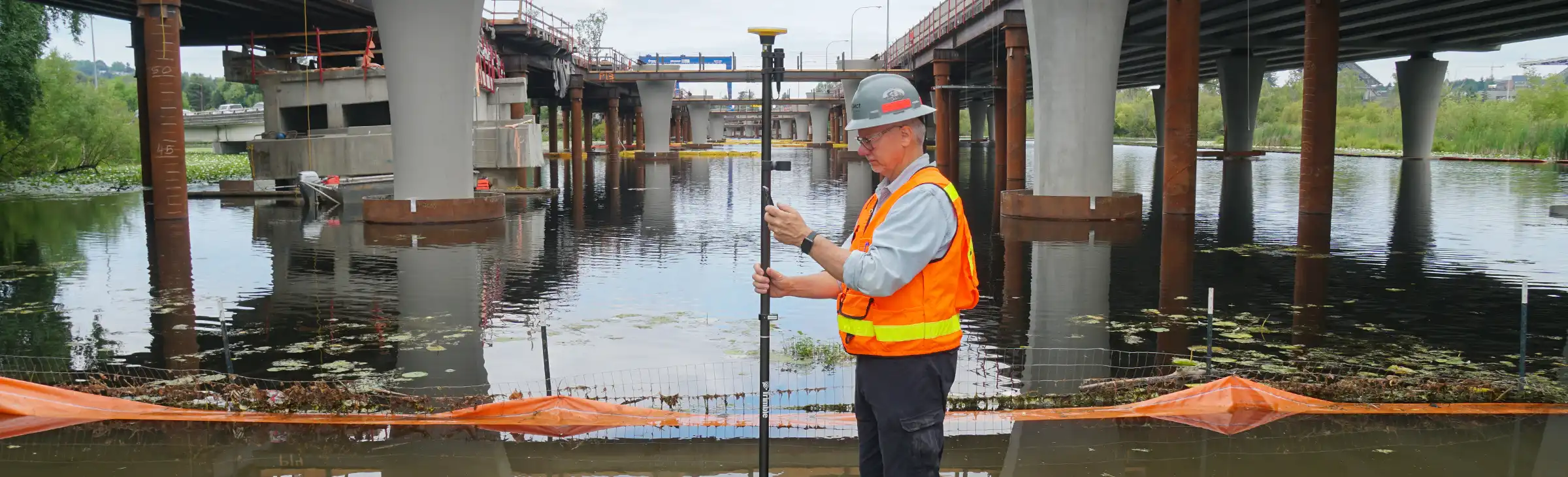 Man standing with a GNSS receiver near a flooded highway overpass.