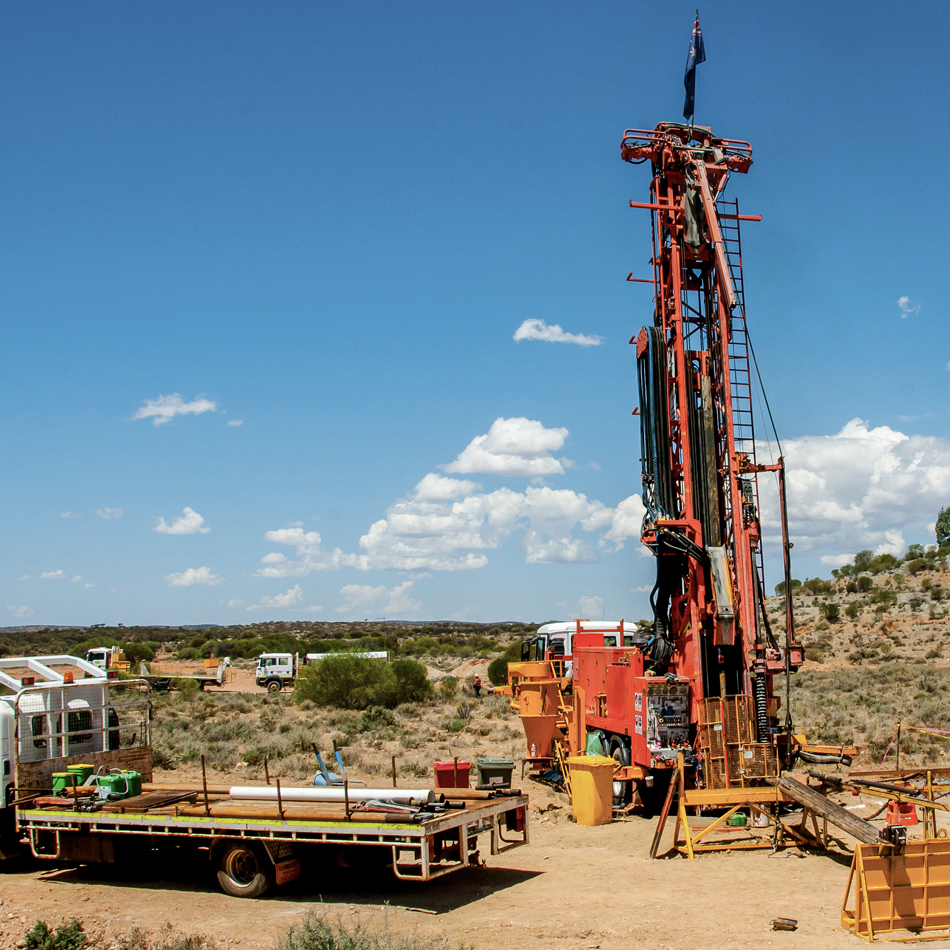 A large red drill rig is positioned in an open area of a mining site