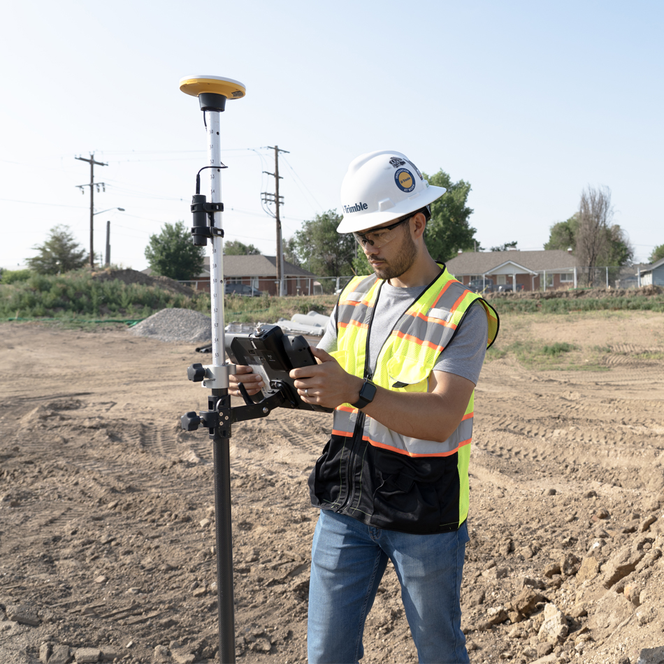 测绘人员身着反光背心操作搭载 DA2 接收机的 Trimble Catalyst 系统