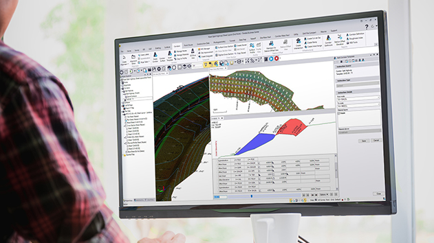 Desktop monitor in an office displaying Trimble Business Center software 2D and 3D models for a highway roading project