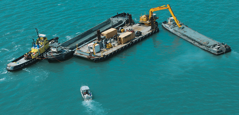 Aerial view of a productive marine dredging operation using an excavator, barges, and a hydrographic survey boat