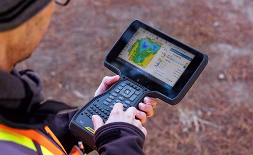 Man holding a Trimble TSC7 survey controller showing Trimble Access software on its screen.