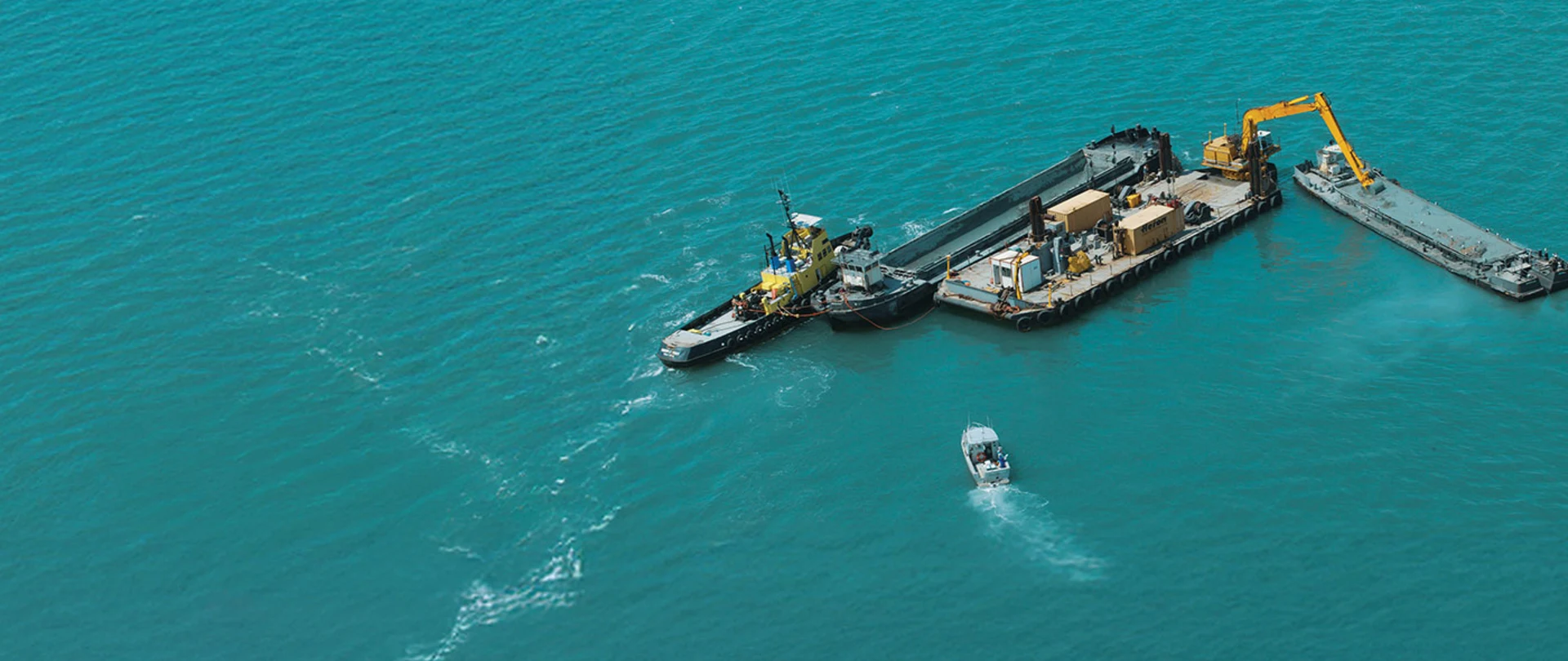 Aerial view of a productive marine dredging operation using an excavator, barges, and a hydrographic survey boat