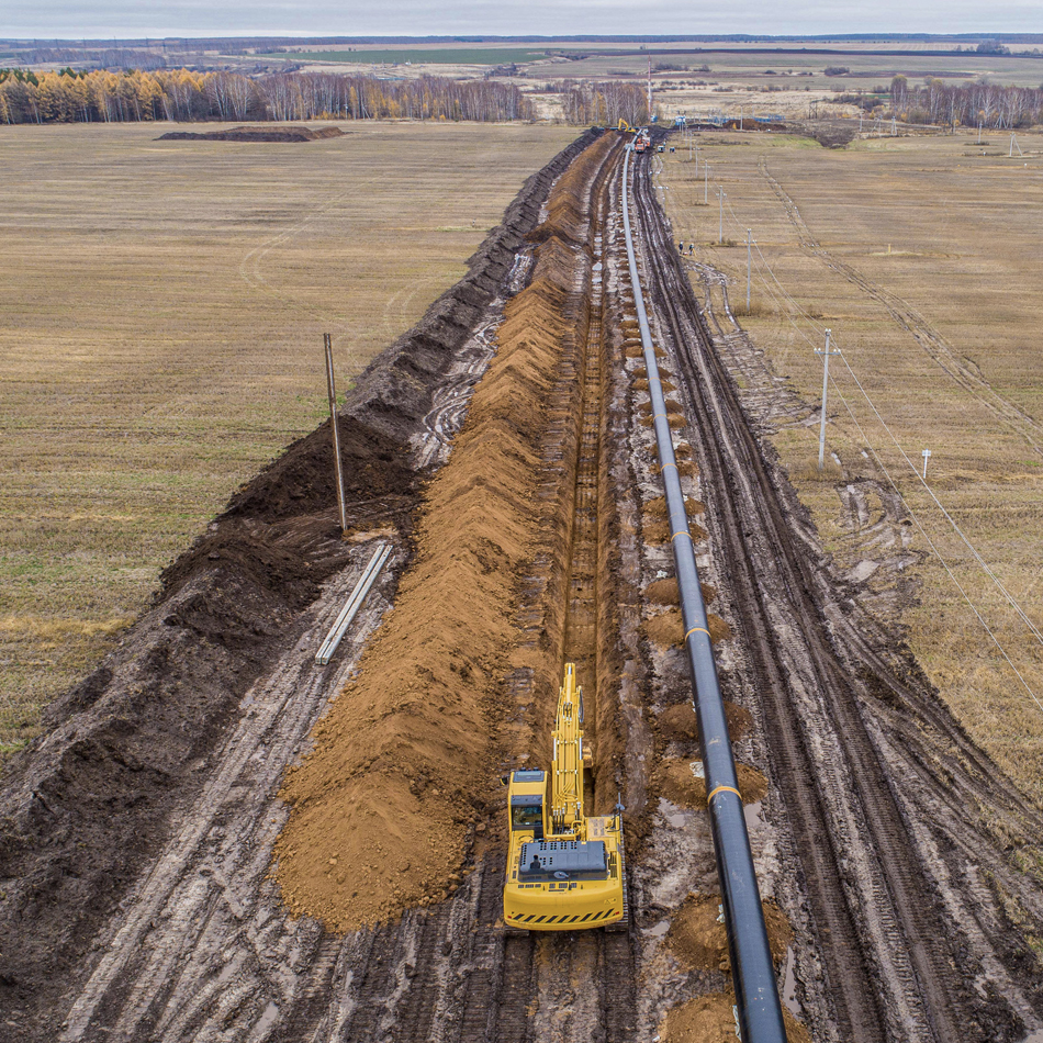 A construction site scene showing a bulldozer next to a large pipe, surrounded by dirt and debris