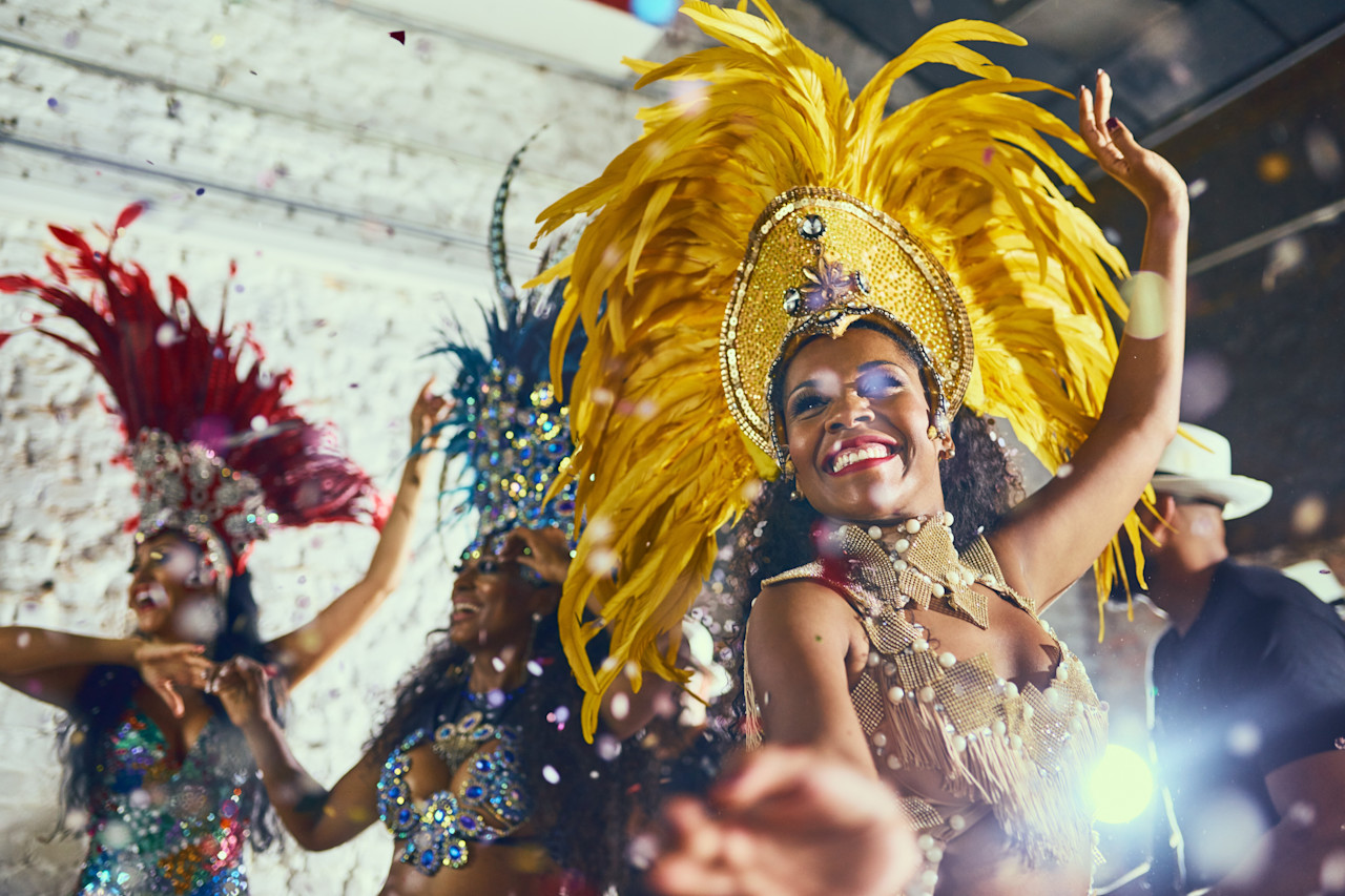 Dançarinas de samba sorrindo e dançando com confetes ao redor.
