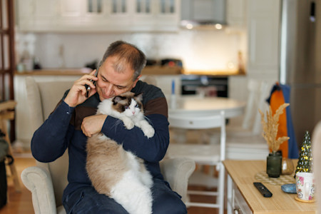 Mature man chatting with friends while bonding with his pet at home 
