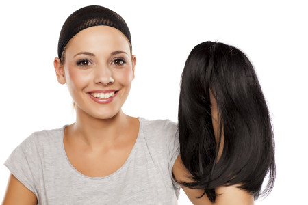 Smiling girl with alopecia areata wearing a wig cap and holding her wig