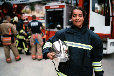 Female firefighter standing near fire truck with helmet in hand