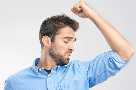 Young man with hyperhidrosis lifting his arm to smell his underarm