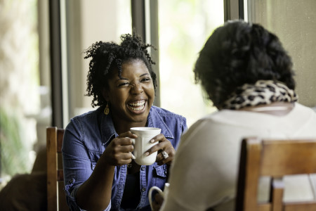 Black women laughing over coffee.