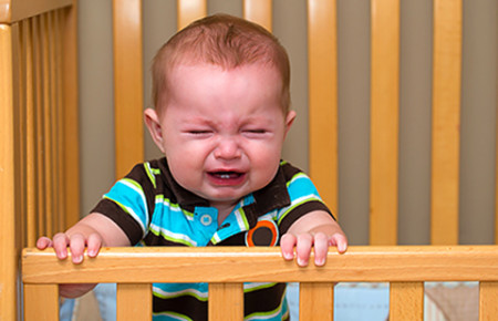 Baby crying in crib. Itchy eczema can cause sleep loss. 