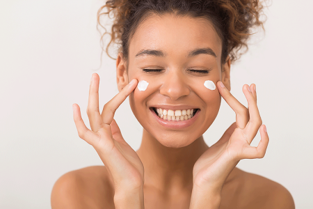 Smiling young woman applying moisturizing cream on her face