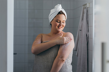 A woman is placing moisturizer on her skin while taking GLP-1 drugs for weight loss.