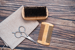 Beard kit with scissors, comb, and brush on wooden background.