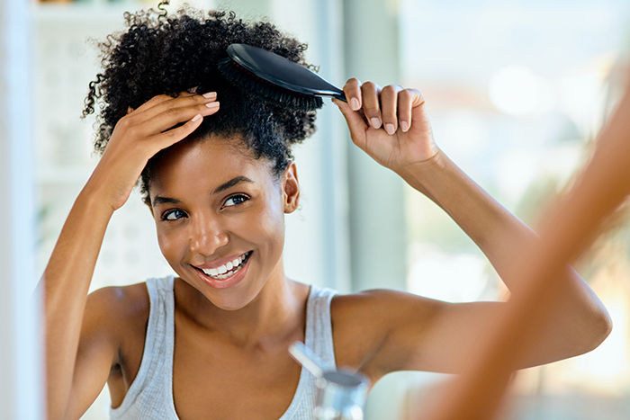 Woman with natural hair smiling while brushing her hair