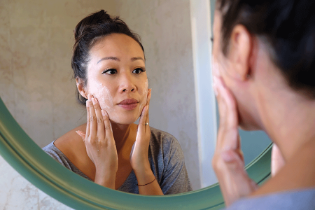 Woman looking in mirror while applying cream to rash on face