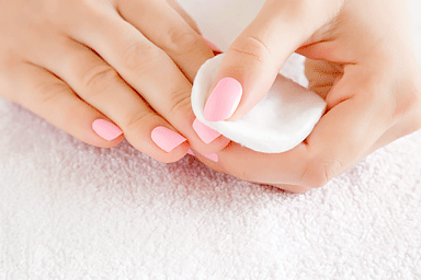 Woman removing pale pink gel nail polish from her fingernails