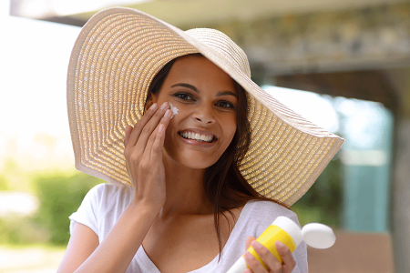 Woman wearing wide-brimmed hat and applying sunscreen to her face