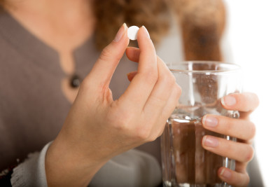 Close-up of female hands holding one pill and glass of water