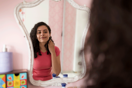 Happy teenager looking in her bedroom mirror