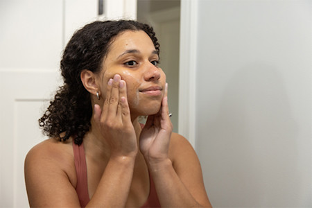 Woman applying a skin care product to her face in the mirror using her fingertips 