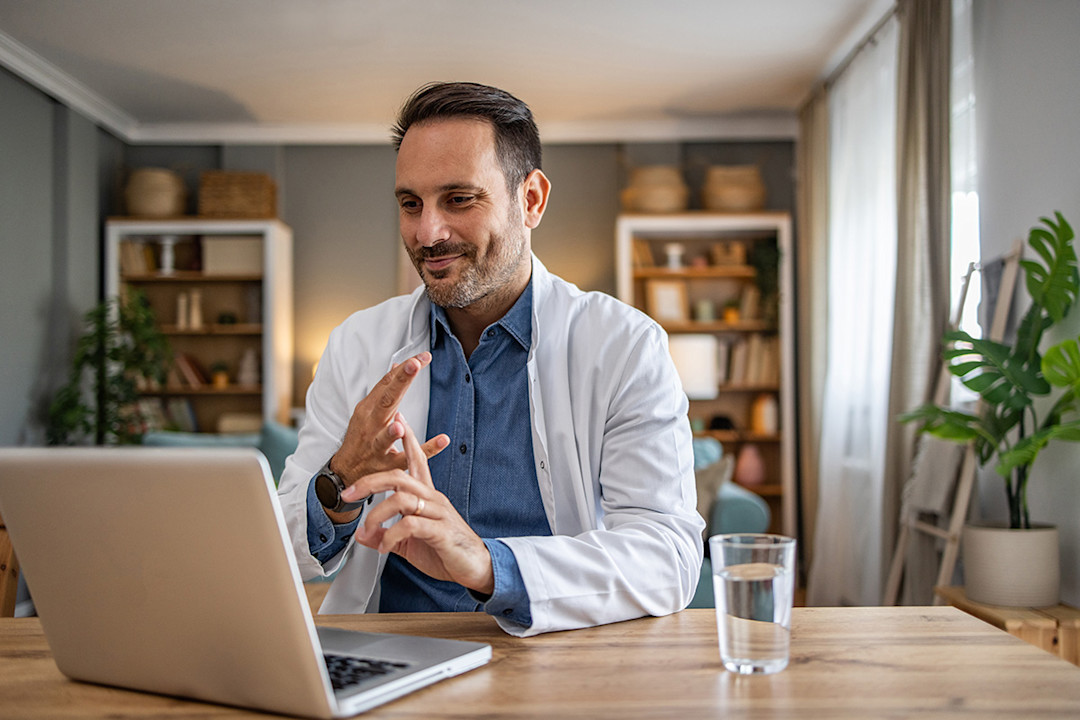 Male doctor sitting in front of laptop attending virtual town hall for AADA.