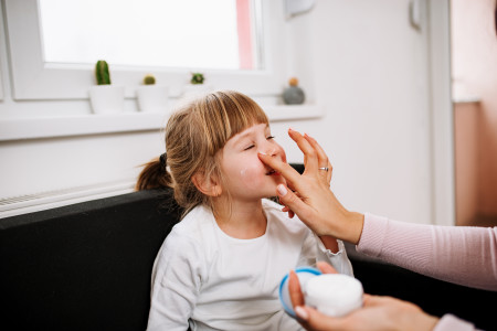 mother putting lotion on child's cheek