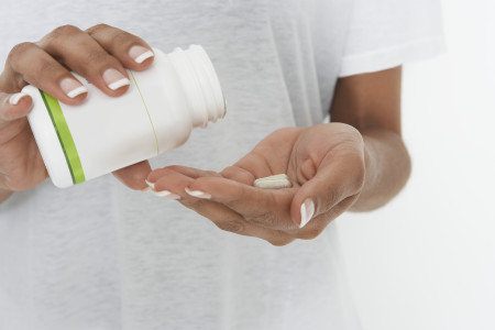 Woman skin of color holding bottle of pills, mid section
