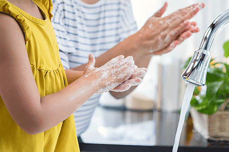 Mom helps her young daughter wash her hands. They are rubbing their hands together creating foam with the soap.
