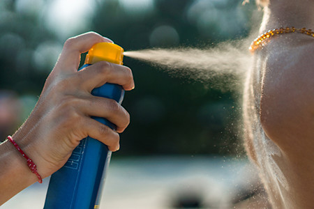 Image of a woman using a stick and spray sunscreen