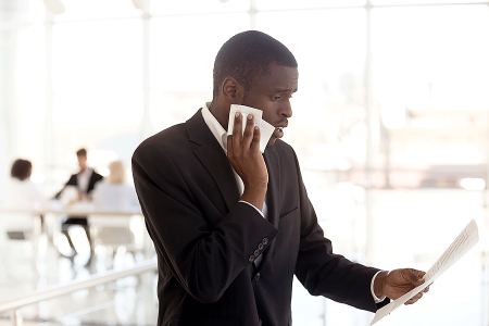 Man with hyperhidrosis wearing a suit, standing away from his coworkers, and holding a towel to his face