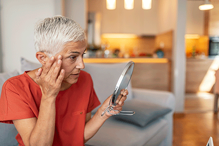 Older woman looking in mirror at her aging skin.