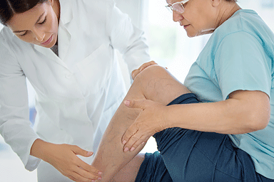 Side view of female dermatologist examining legs and calves of a senior female patient
