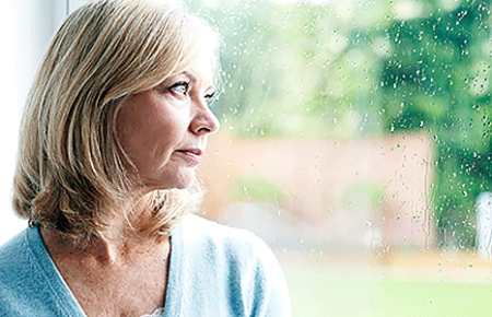 Worried woman looking out window during a rain shower
