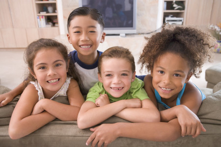 4 smiling children leaning on the back of a couch