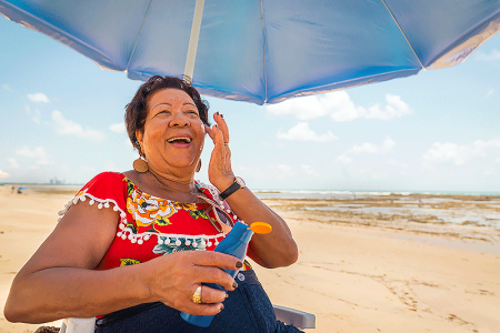 Woman sitting under beach umbrella applying sunscreen to her face