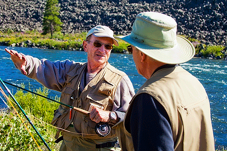 Two fisherman wearing hats, sunglasses, long sleeves, and pants talking outdoors