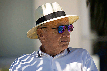 Older man relaxing outdoors in the shade, wearing a hat and sunglasses