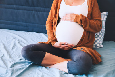 Pregnant woman sitting on bed holding hands on belly