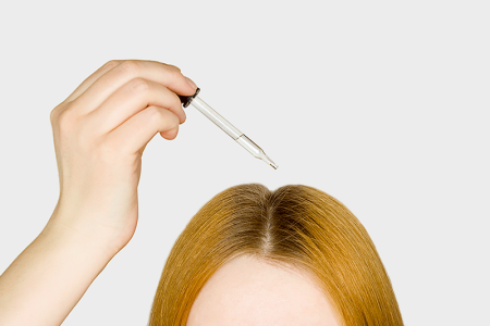 Woman applying scalp medication to top of her head.