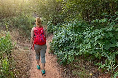 A woman walking through the forest with poison ivy surrounding her. 