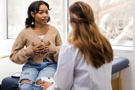 Dermatologist telling her teenage patient about what can cause hyperhidrosis