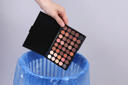 Hand throwing eye shadow palette into trash bin