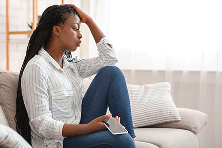 Black woman sitting on her couch, resting her head in her hand