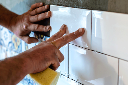 Close-up of man’s hands installing tiles, a type of work that can cause dyshidrotic eczema.