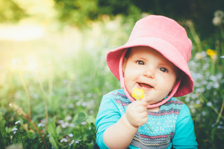 A baby outside holding a flower